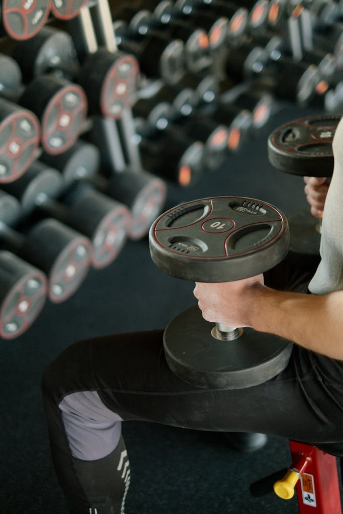 A person lifting dumbbells while sitting on a bench in a modern gym setting.