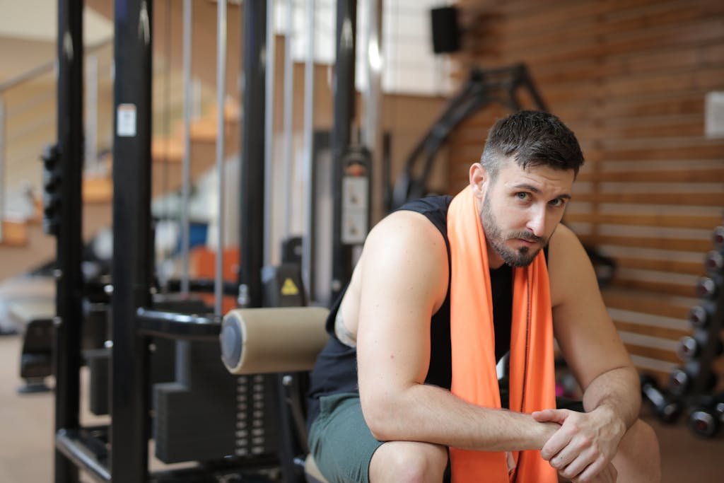 Adult male resting in a gym with an orange towel after strength training.