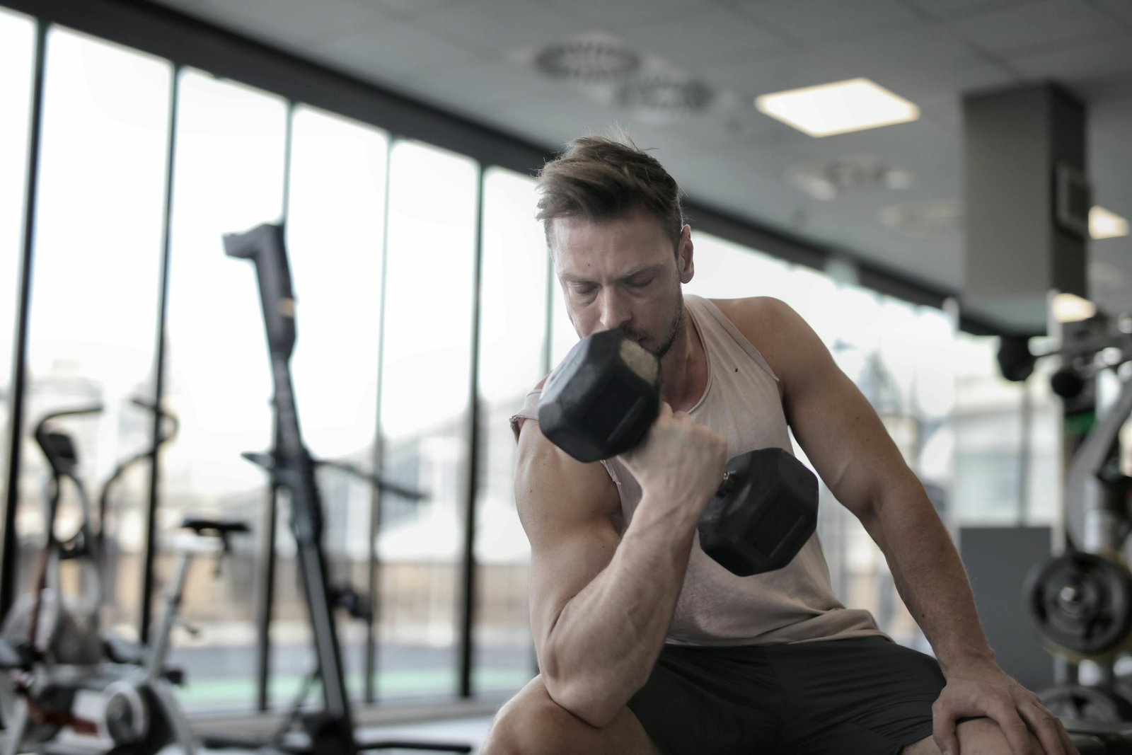 Treinos Rápidos que Ajudam a Reduzir a Ansiedade 1 Low angle of powerful male athlete in sportswear performing exercise with heavy metal dumbbell while sitting on bench during workout in modern gym